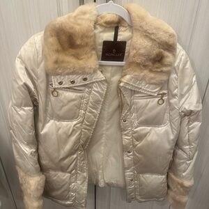 Pearly white Moncler women's jacket with fur collar and gold details.
